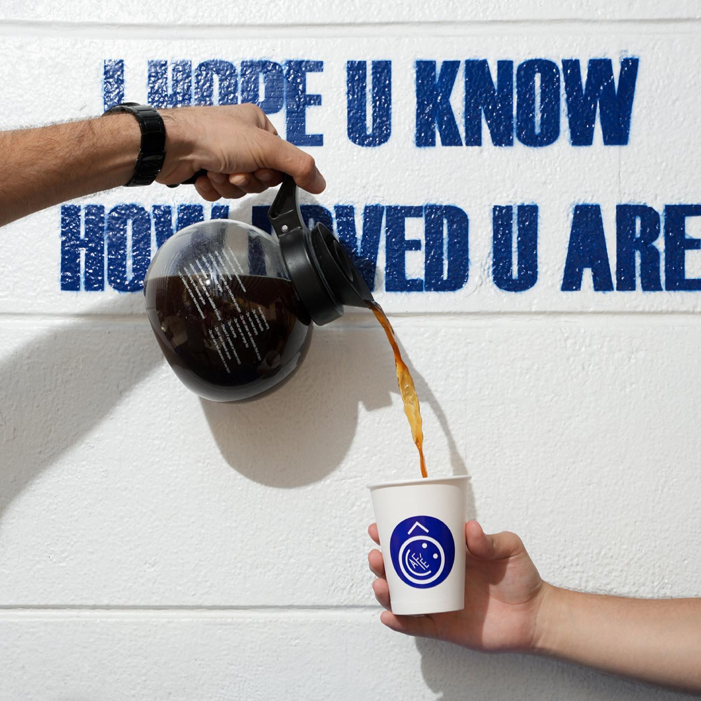 A carafe pouring filter coffee into an Ô café cup against a stencilled white wall